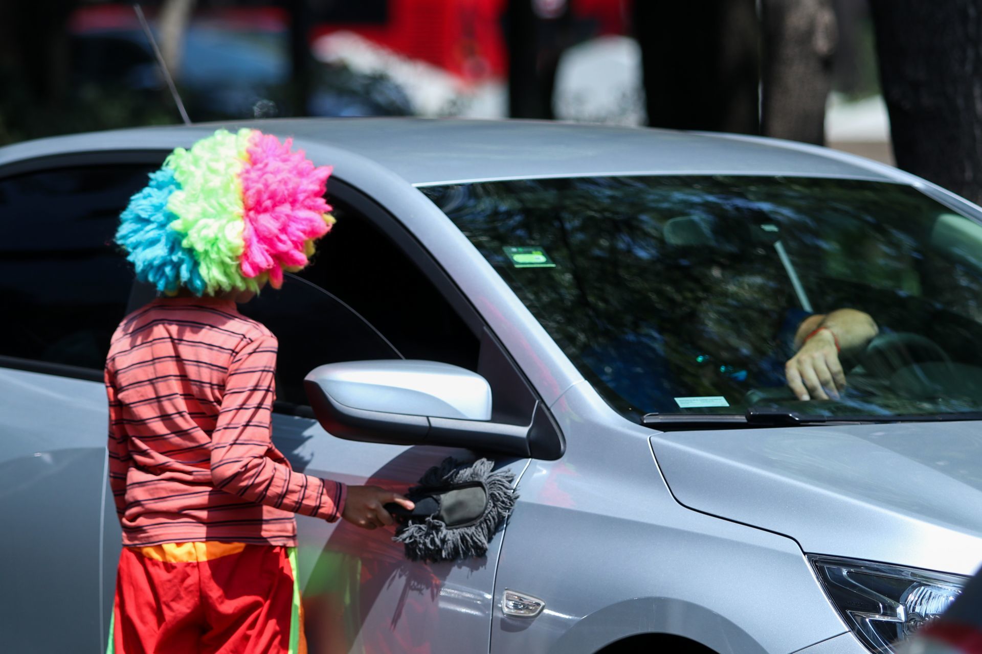 Niño disfrazado de payasito, trabajando como limpiaparabrisas