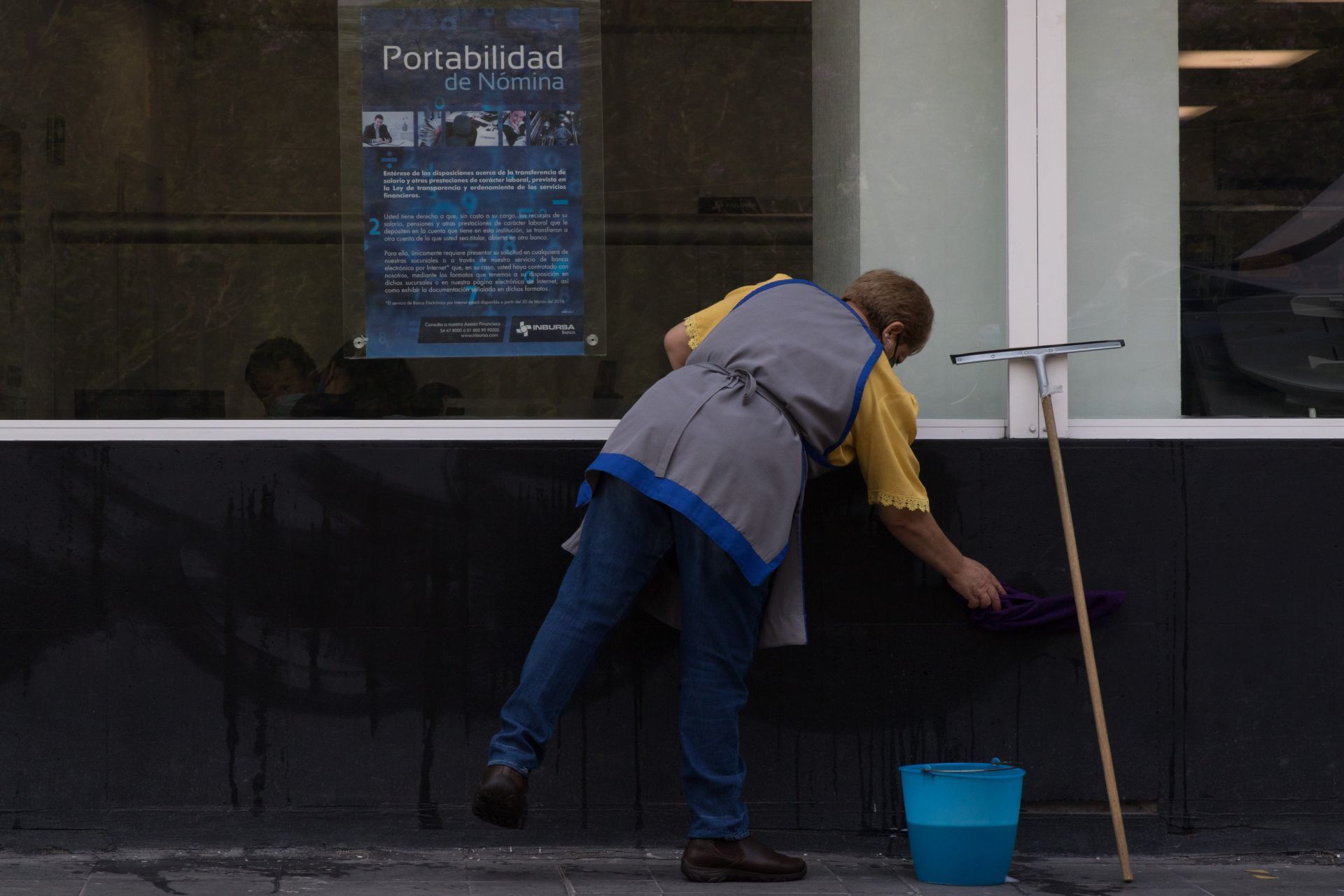 Trabajadora limpiando la parte de afuera de un banco