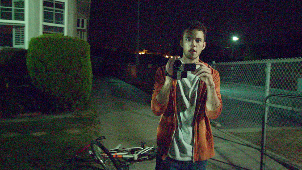 Se ve a un adolescente parado con una cámara en la calle durante la noche